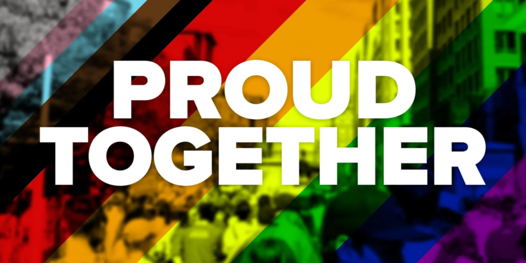 The image features the words "PROUD TOGETHER" in large, bold, white letters against a blurred background. The background incorporates the colors of the Pride flag (red, orange, yellow, green, blue, purple) overlaid on a crowd of people, suggesting a Pride march or celebration. The image evokes a feeling of unity, pride, and visibility.